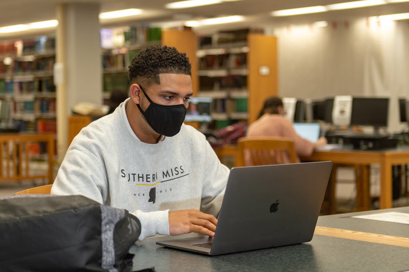 Photo of Black Student in Library Wearing USM Hoodie and Mask