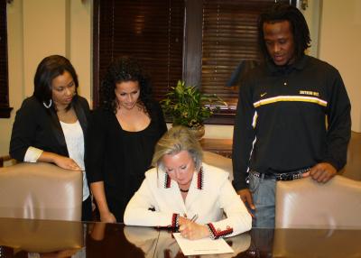 Southern Miss President Martha Saunders signs a proclamation endorsing the Student-Athlete Advisory Committee's (SAAC) participation in the Conference USA Changing Lives community service program as students Alyssia Cole, Danielle La Pointe and Ronnie Thornton look on.