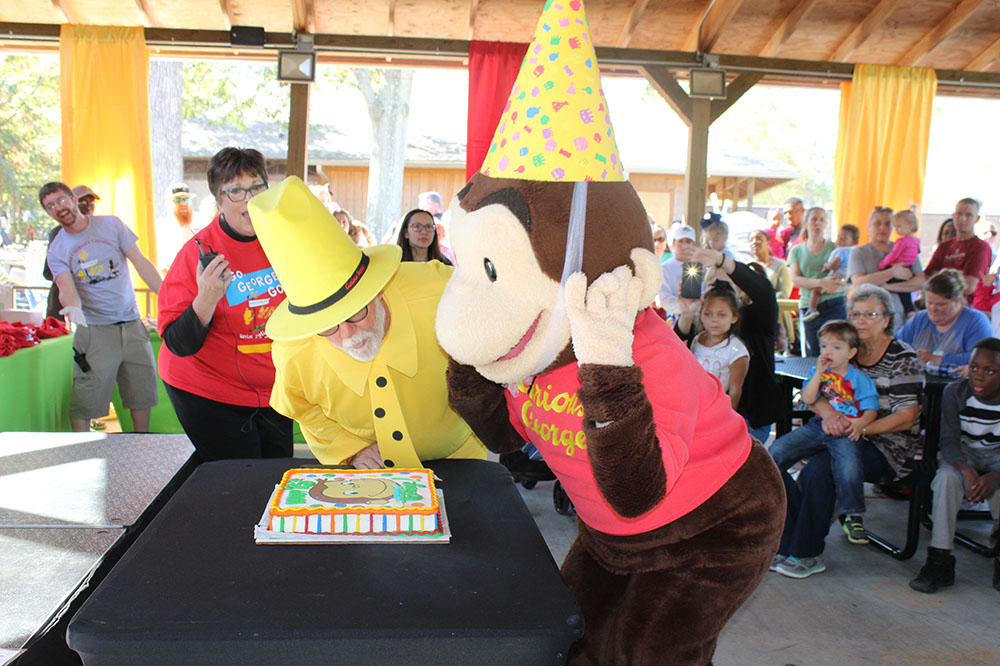 Curious George character blowing out candles on a cake