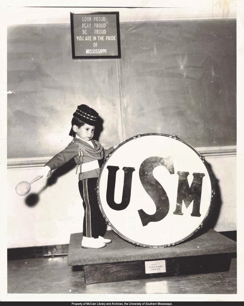 Little boy playing drums that have USM on them