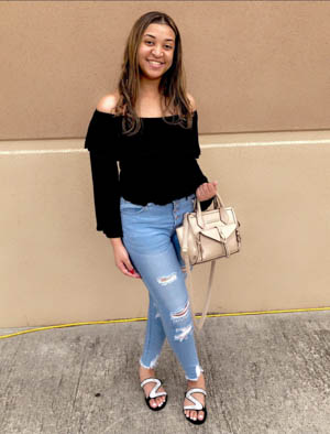 Willica McClendon, young black-looking woman smilling and holding purse, wearing black shirt, holey jeans, and sandals