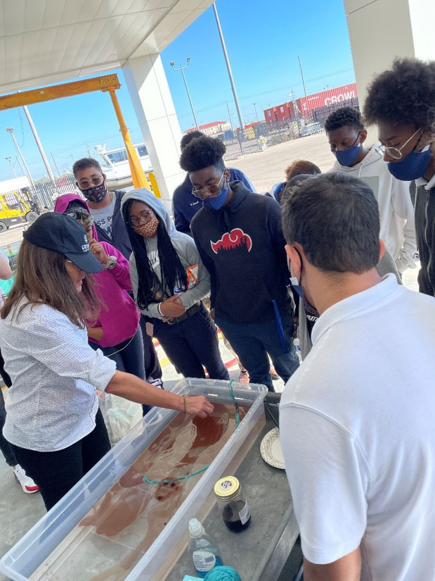 On a GenSea field trip to the Marine Research Center, Tara Skelton demonstrates to engineering students from Moss Point HS the tools emergency responders must choose from to clean up an oil spill at sea. (Photo credit: Heather Richey, School of Ocean Science and Engineering, USM)