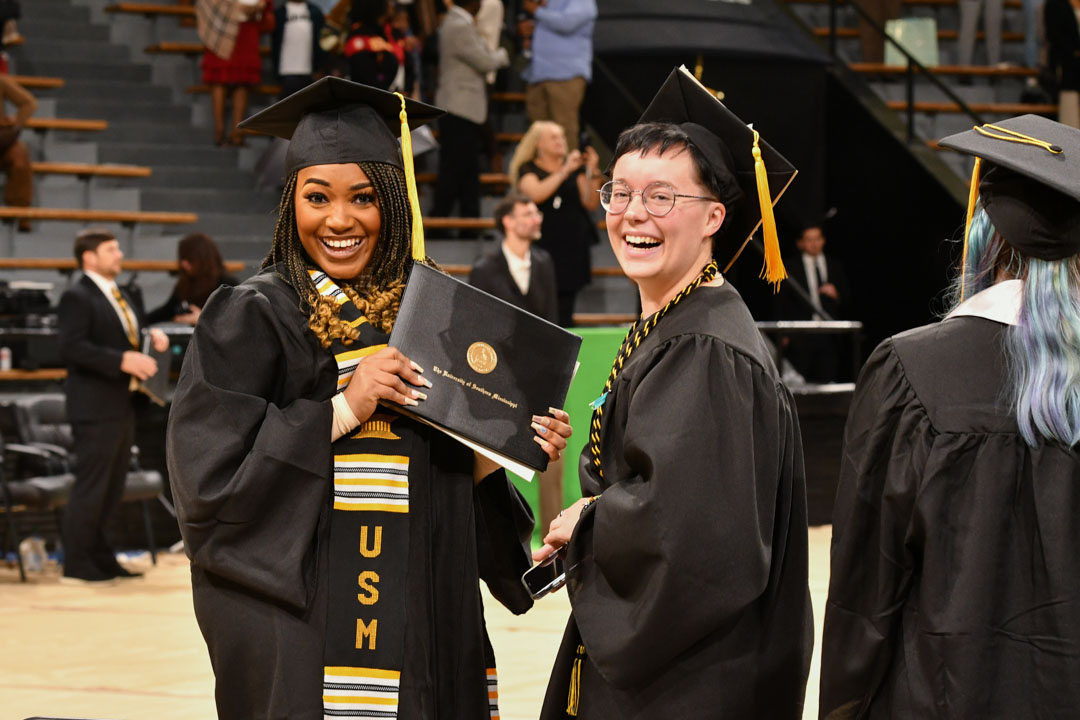 Students smile with their diplomas at commencement. 